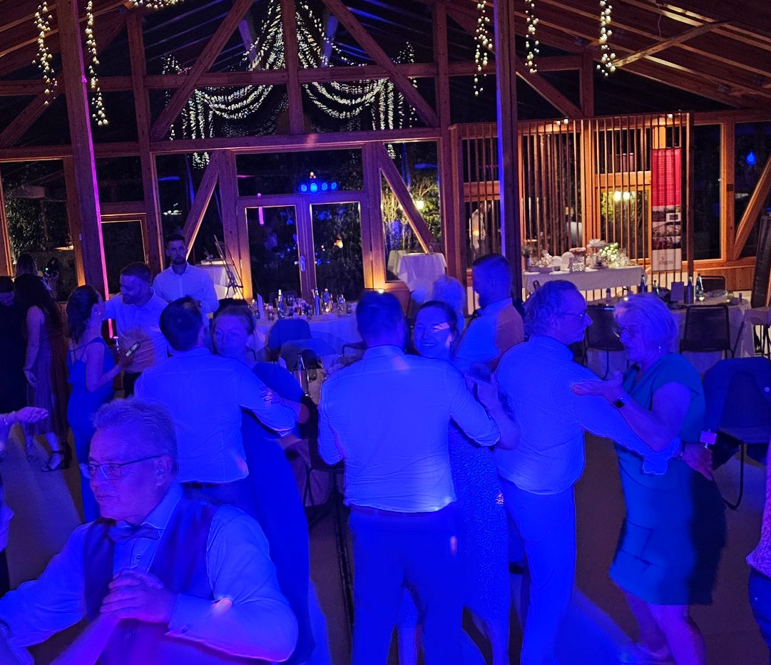 Fliedertreiberei Engler Tanzende Menschen in einem festlichen Ambiente, blau beleuchteten Raum mit Dekoration.